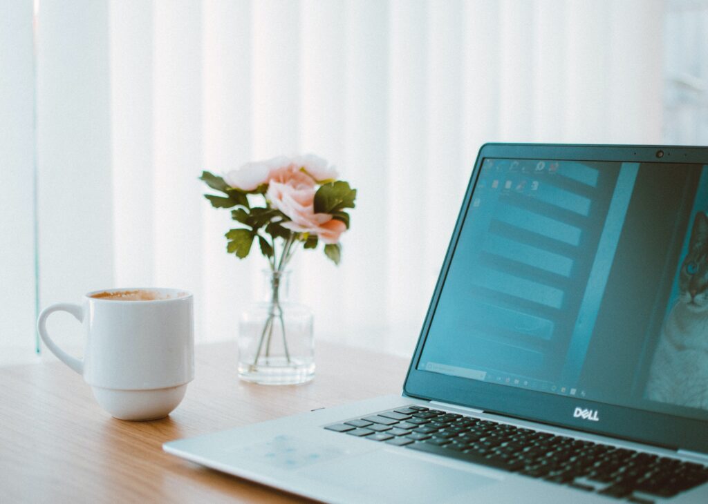 A cozy workspace with a laptop, coffee cup, and a flower vase.